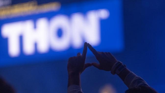 A person in the shadow raises their hands in the shape of a diamond in the foreground of a lit "THON" sign