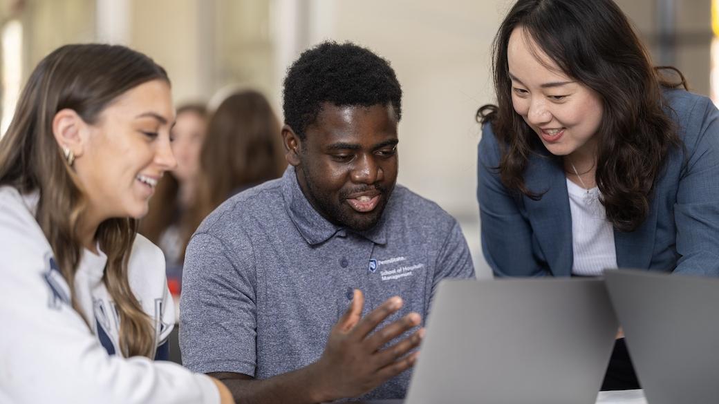 Two students and professor in the College of Health and Human Development work over a laptop. 