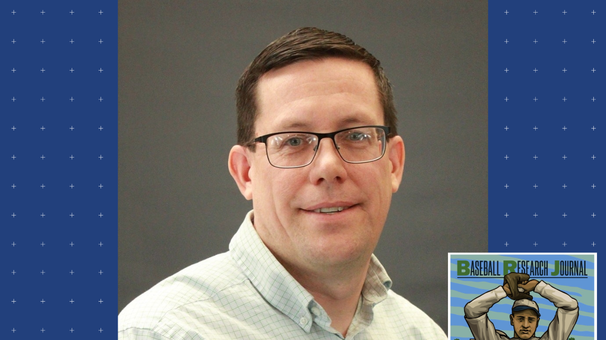photo of man with short straight brown hair wearing glasses and dress shirt, small inset cover illustration of baseball player