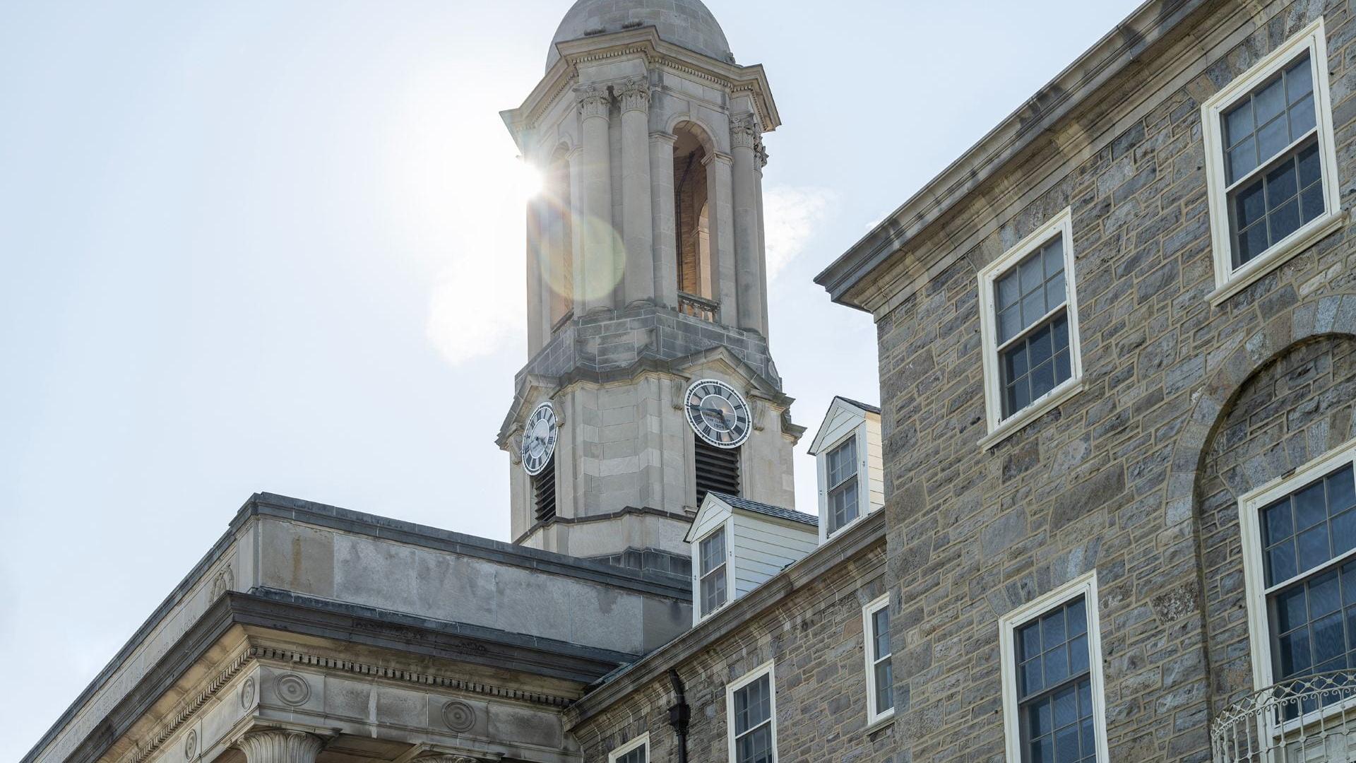 A sunny photograph of the stone bell tower of Old Main against a blue sky.