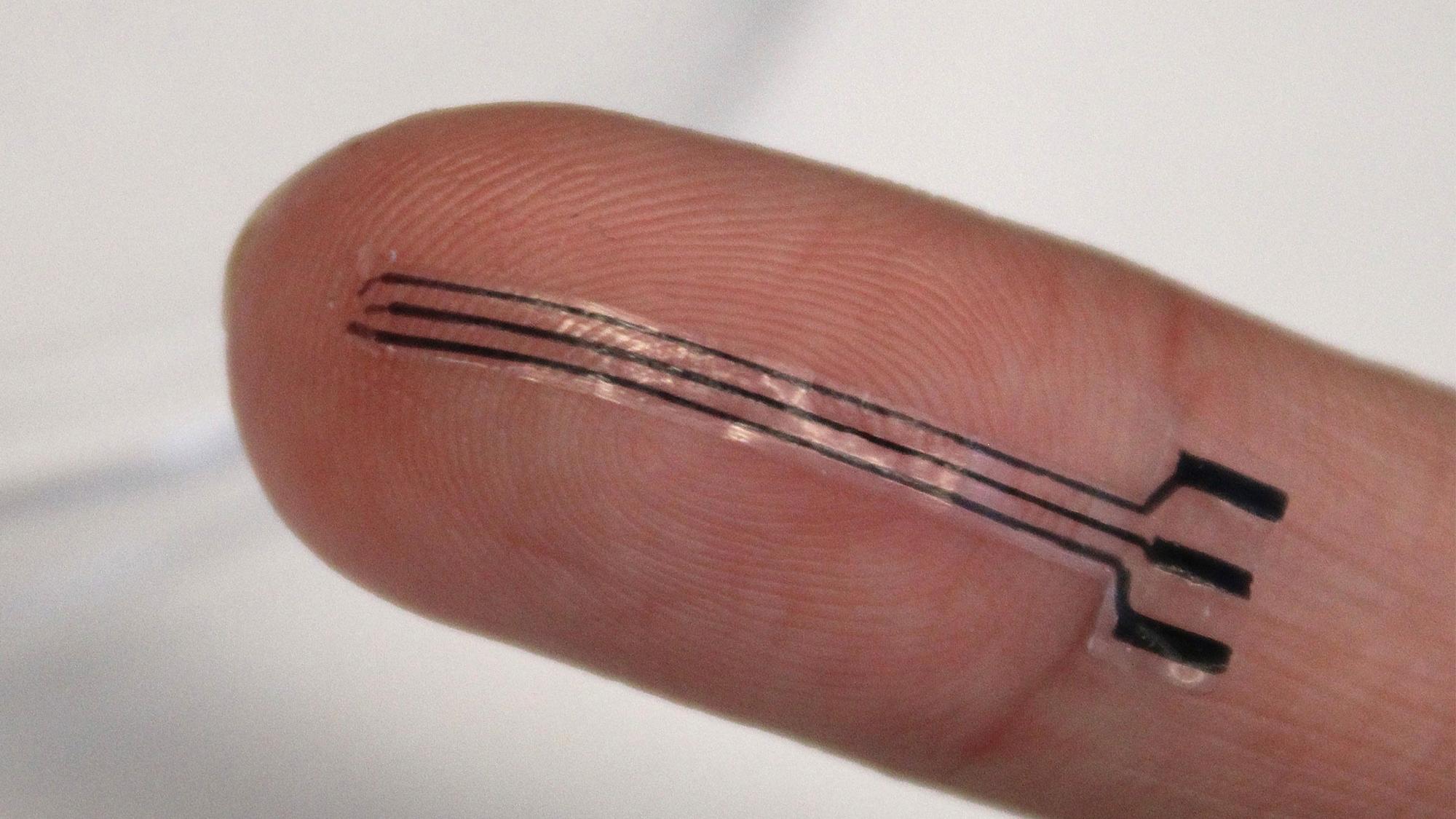A bioelectronic sensor sits laid out on a researcher's fingertip, showing it's small scale.