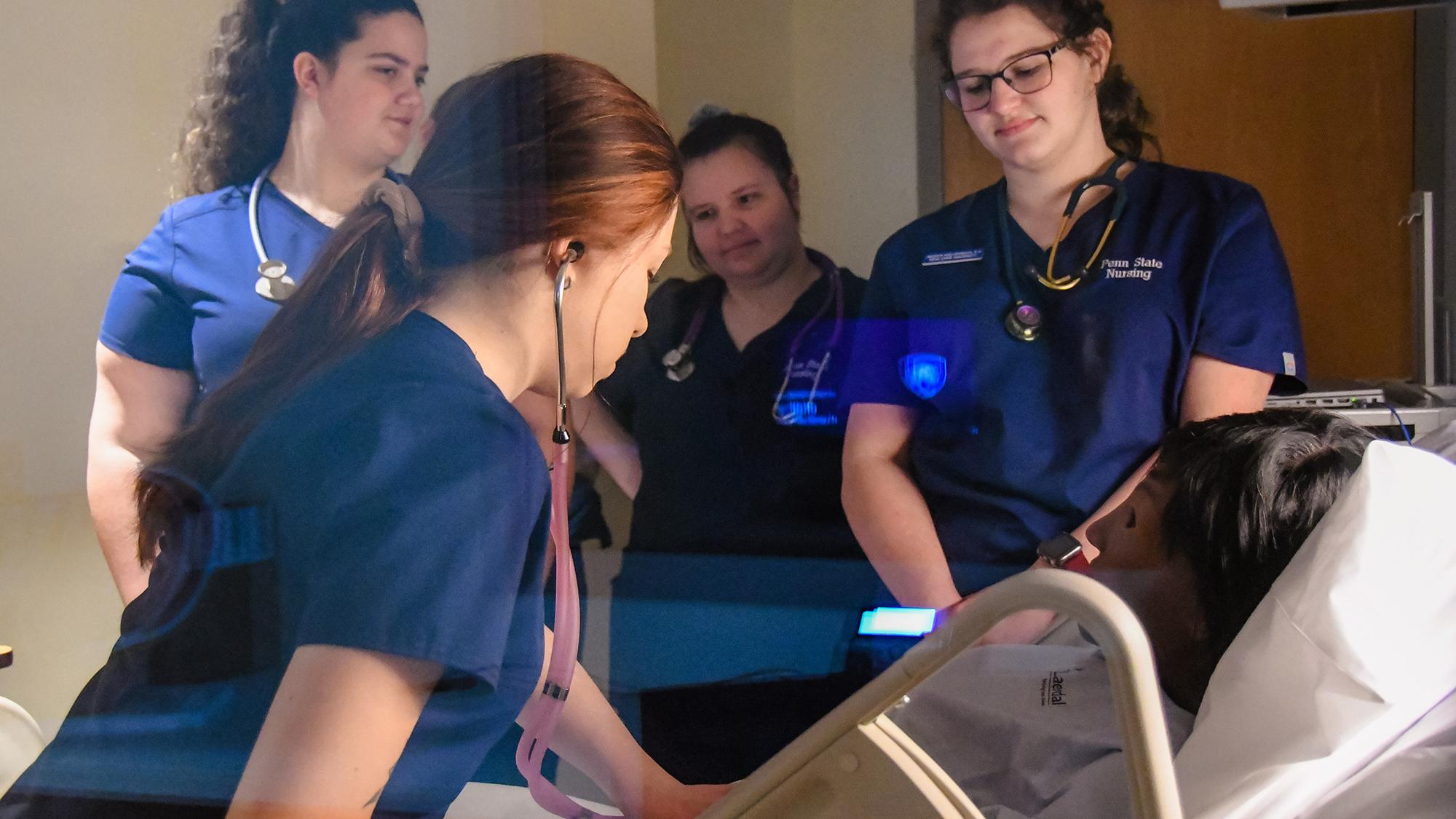 Four nursing students in blue uniforms attend a training manikin