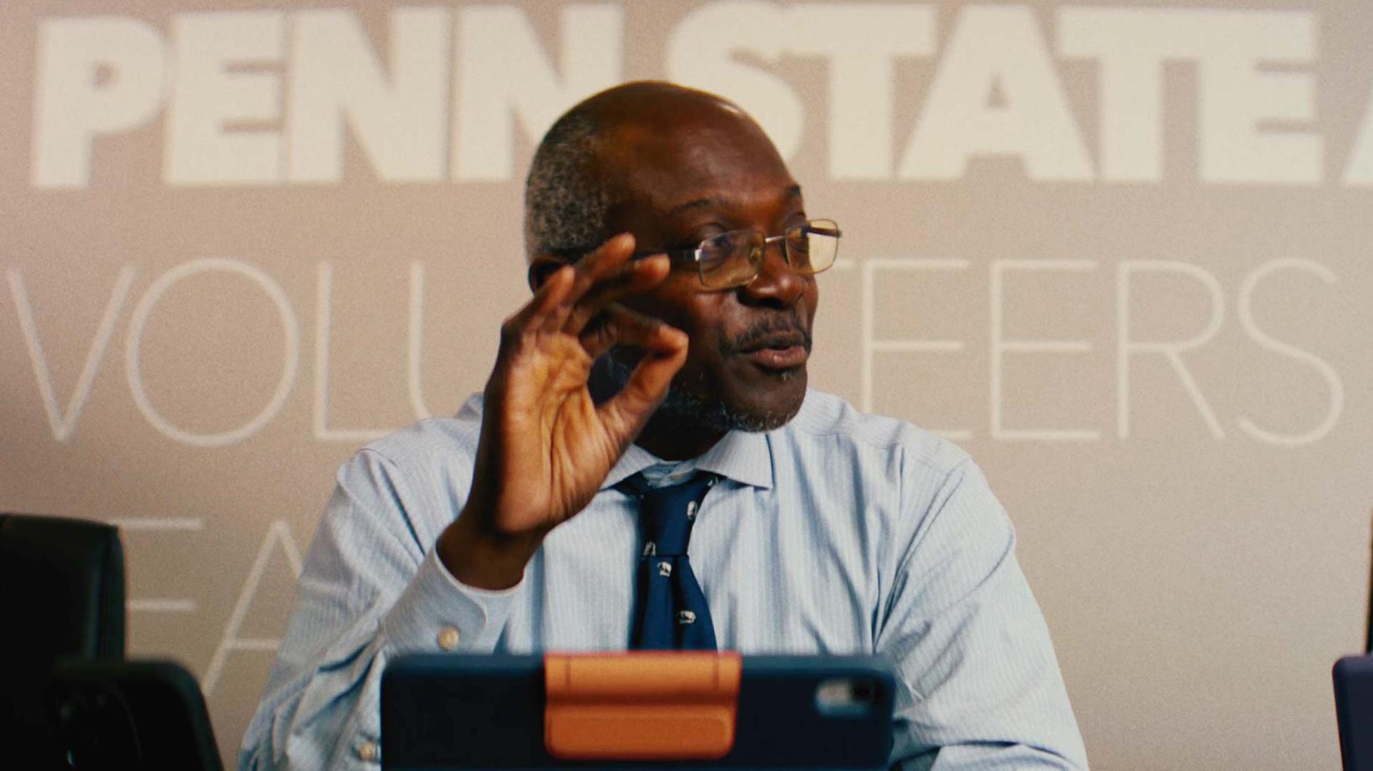 Ron Darbeau sitting at a table with a tablet device in front of him and the words Penn State Volunteers on the wall behind him.