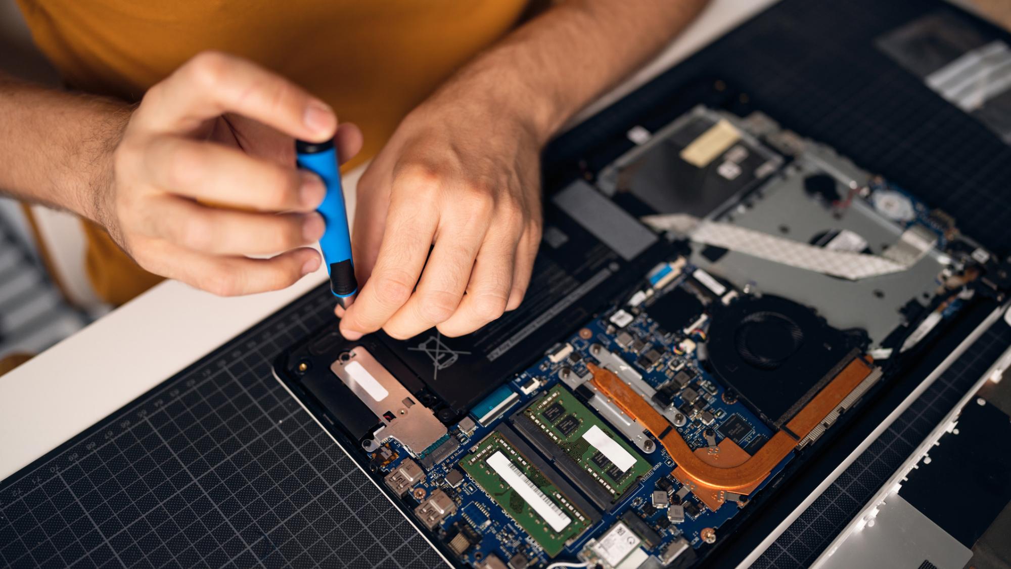 A person with a screwdriver repairing an internal part of a laptop