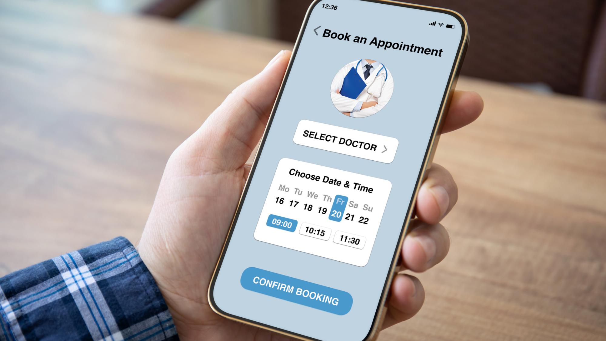 A hand holding a smartphone with a telehealth app on the screen. The app is confirming an appointment booking for Friday, the 20th at 9:00 a.m.