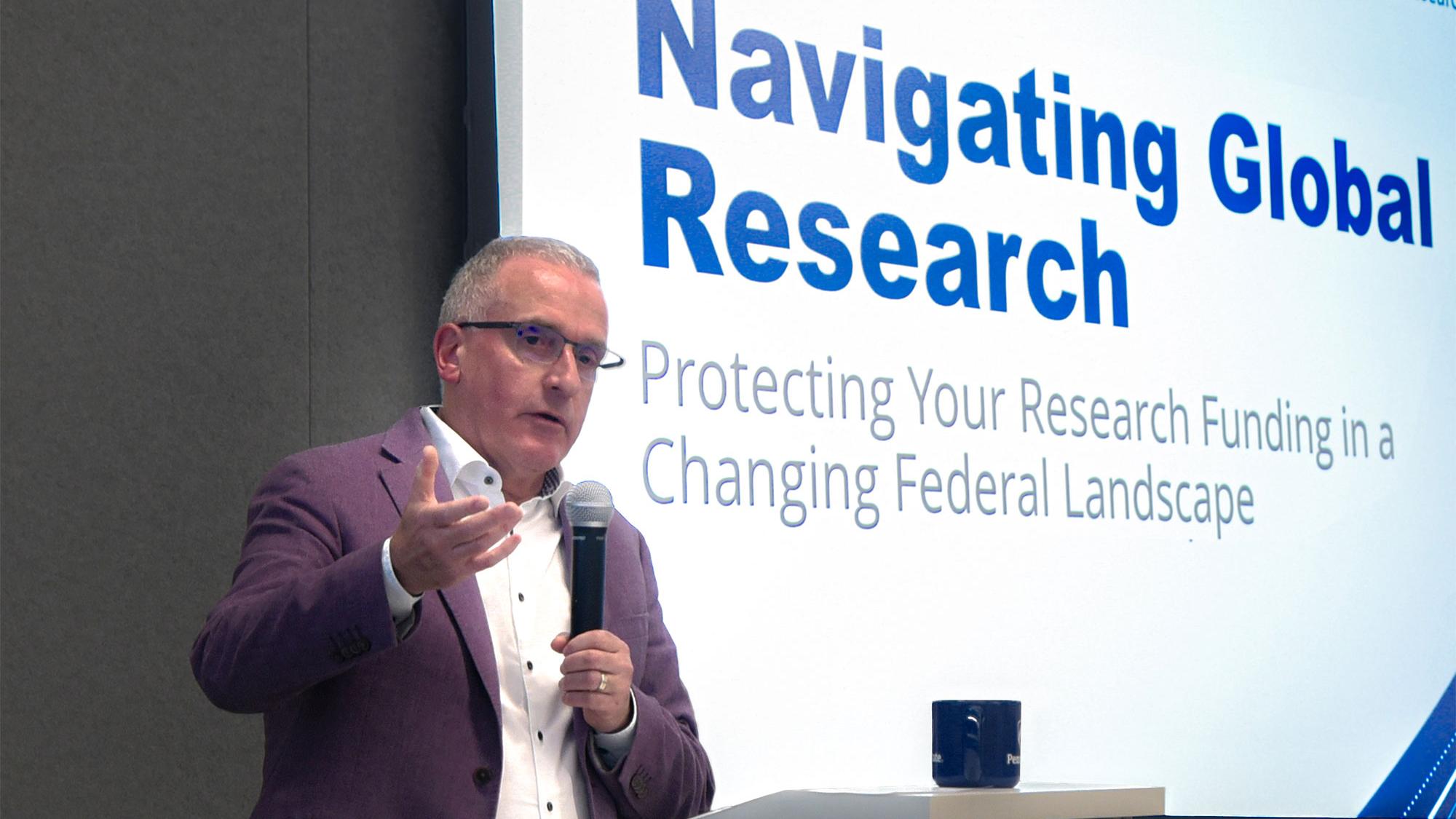 Andrew Read, senior vice president for research, speaking at a podium in front of a slide that reads "navigating global research"