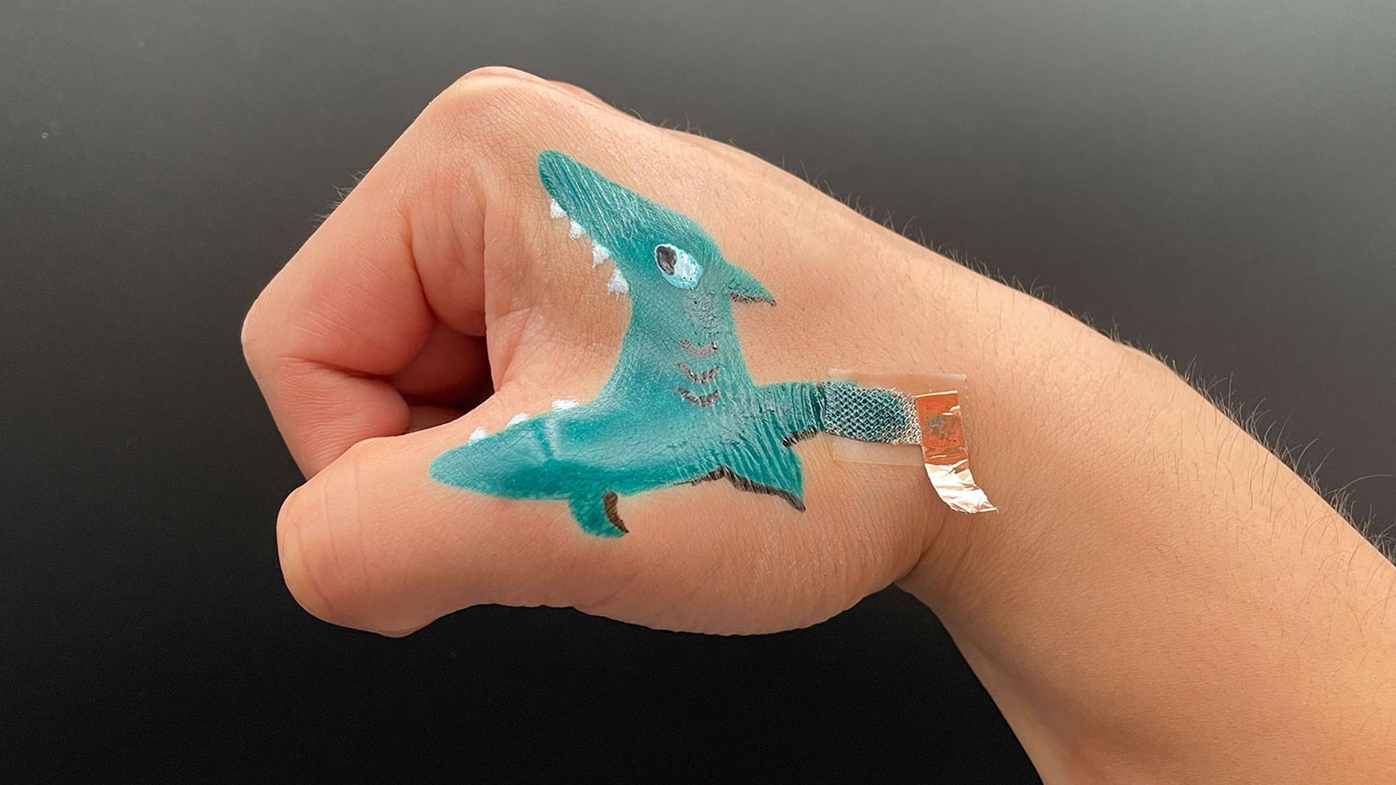 A close up shot of a bioelectrode painted to look like a shark on the side of a researcher's curled fist