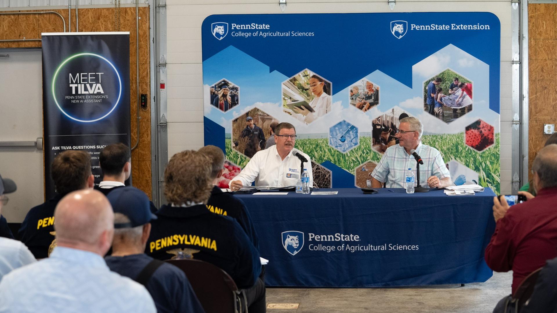 Two men speak on a panel at a Penn State agricultural town hall as an audience listens.