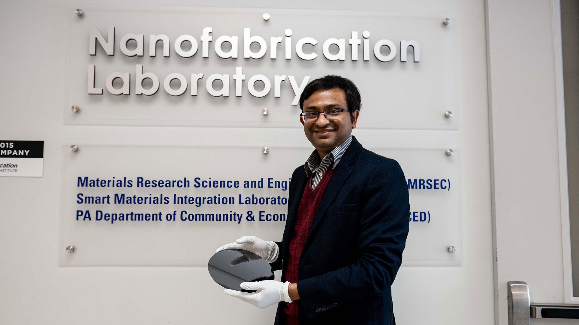 Researcher Saptarshi Das poses in front of the Nanofabrication Lab at Penn State's Materials Research Institute, smiling and holding a silicon wafer used as a foundation in circuit construction