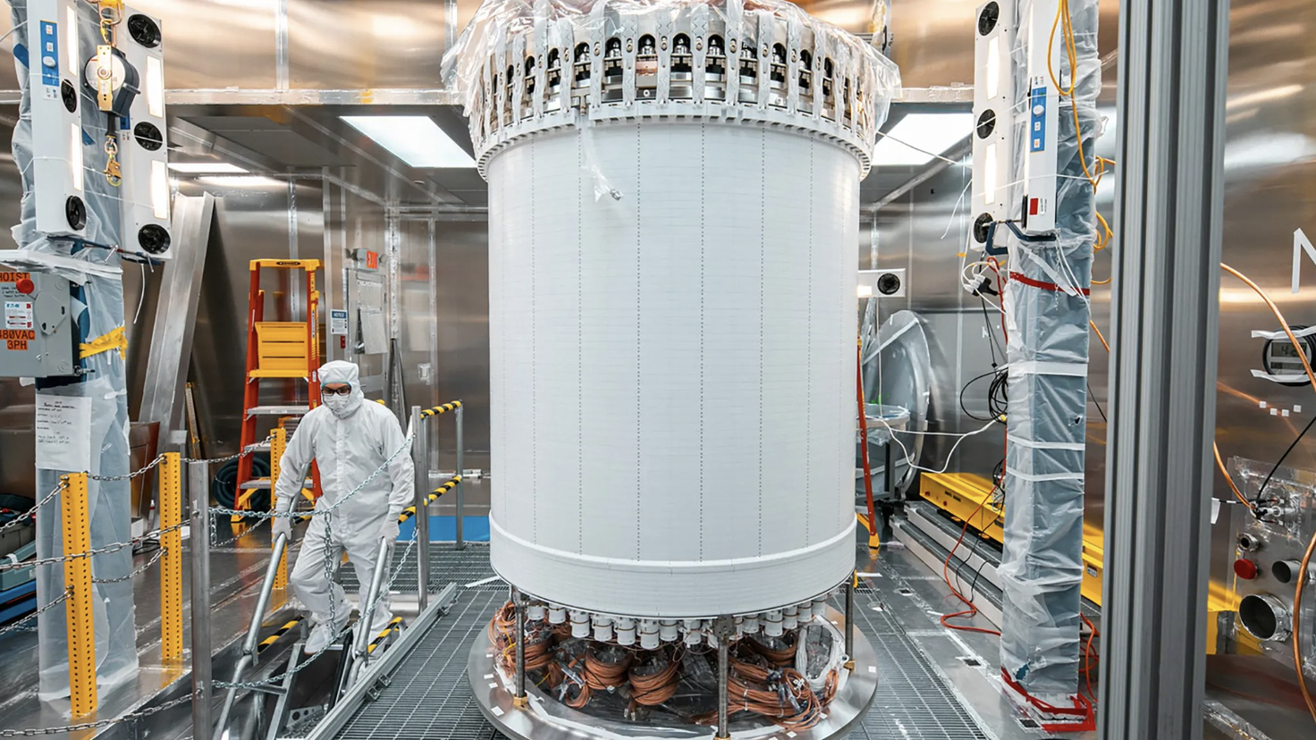 a person in a cleansuit standing by a large while cylindrical machine 