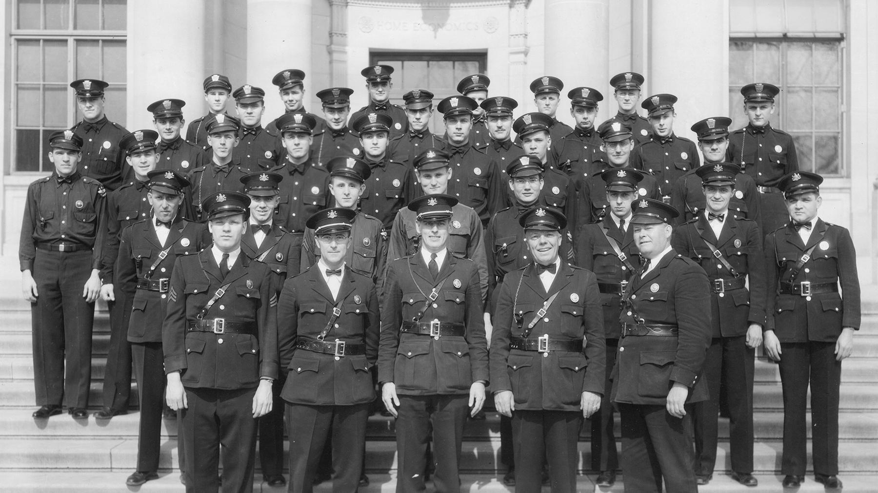 An historic photo of a group of people in uniform posing for a group photo in front of a building