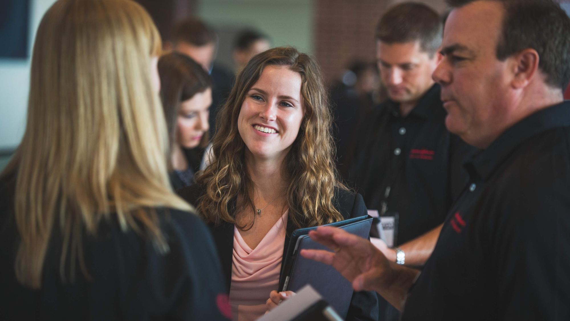 Female student speaking and smiling with employers at the career fair