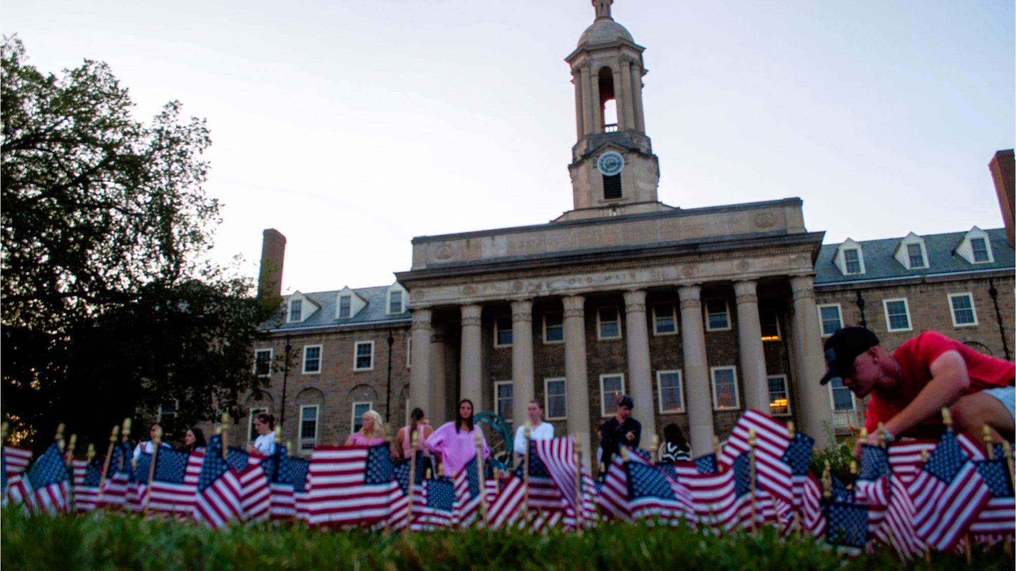 Students place American flags in the grass in front of a campus building