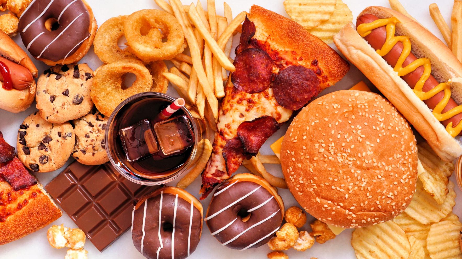 a collection of low quality foods including donuts, french fries, pizza, soda, carmel corn, cookies, and potato chips