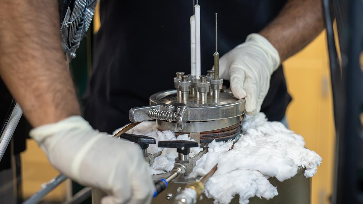 A person wearing gloves closes the lid of a small reaction chamber in a lab. 