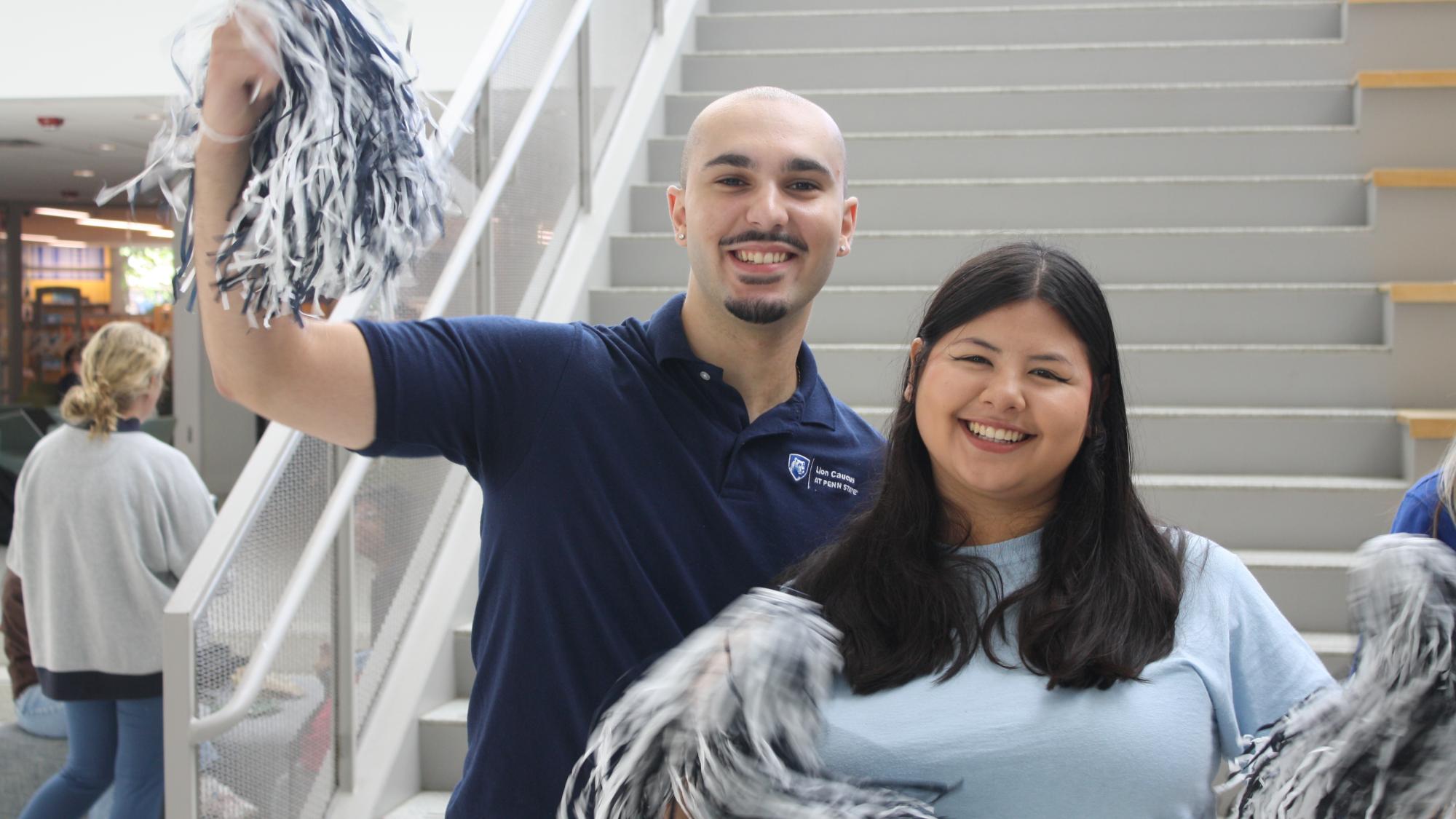 Two students holding blue and white pom poms at an event at Penn State University Park campus