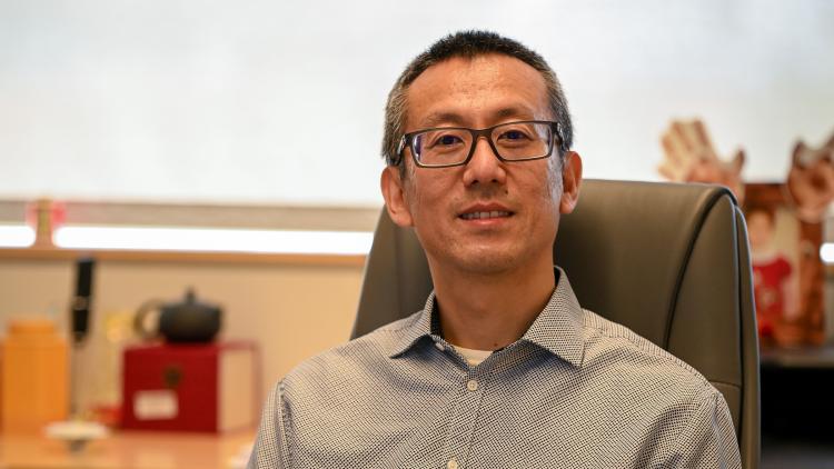 A person in glasses sits at a desk chair.