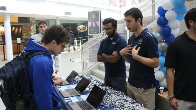 students standing behind a table talking with another student 