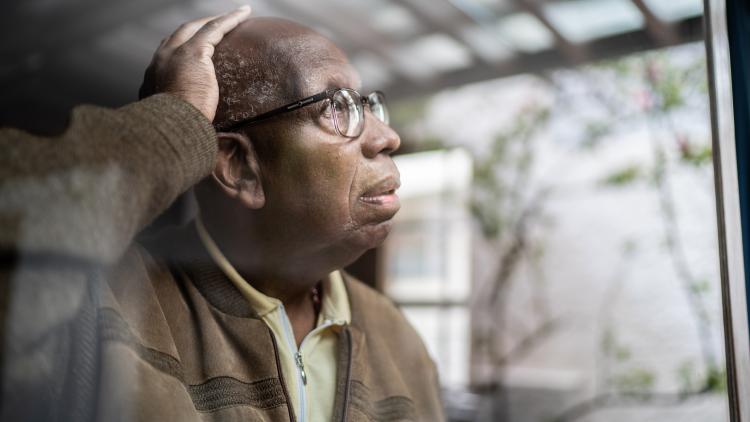 Older man looks concerned as he peers out of his window