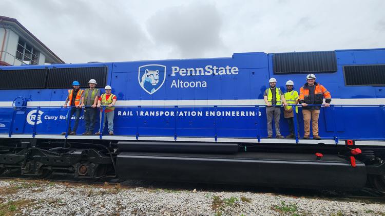 Rail Transportation Engineering students and faculty pose with a Penn State-branded locomotive