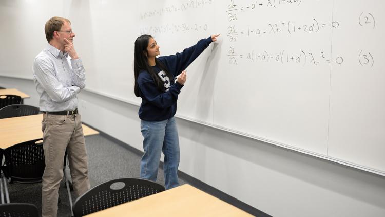 Two people in front of a white board