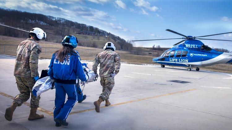 Three people carry a patient to a waiting helicopter