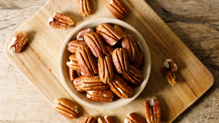 shelled pecans in a bowl on a cutting board