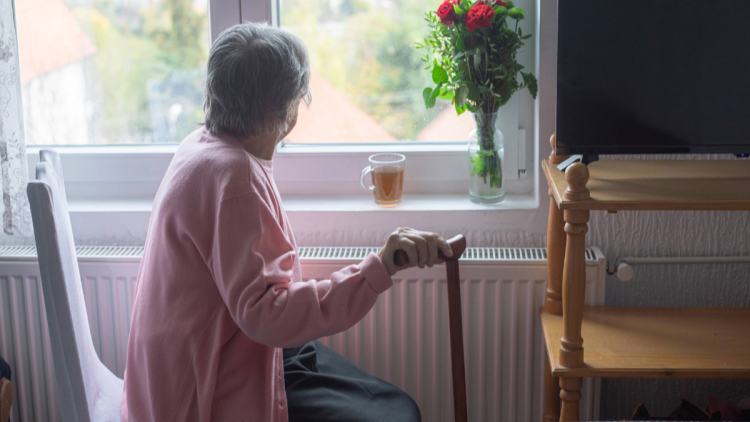 A senior woman holding a cane, looking out a window