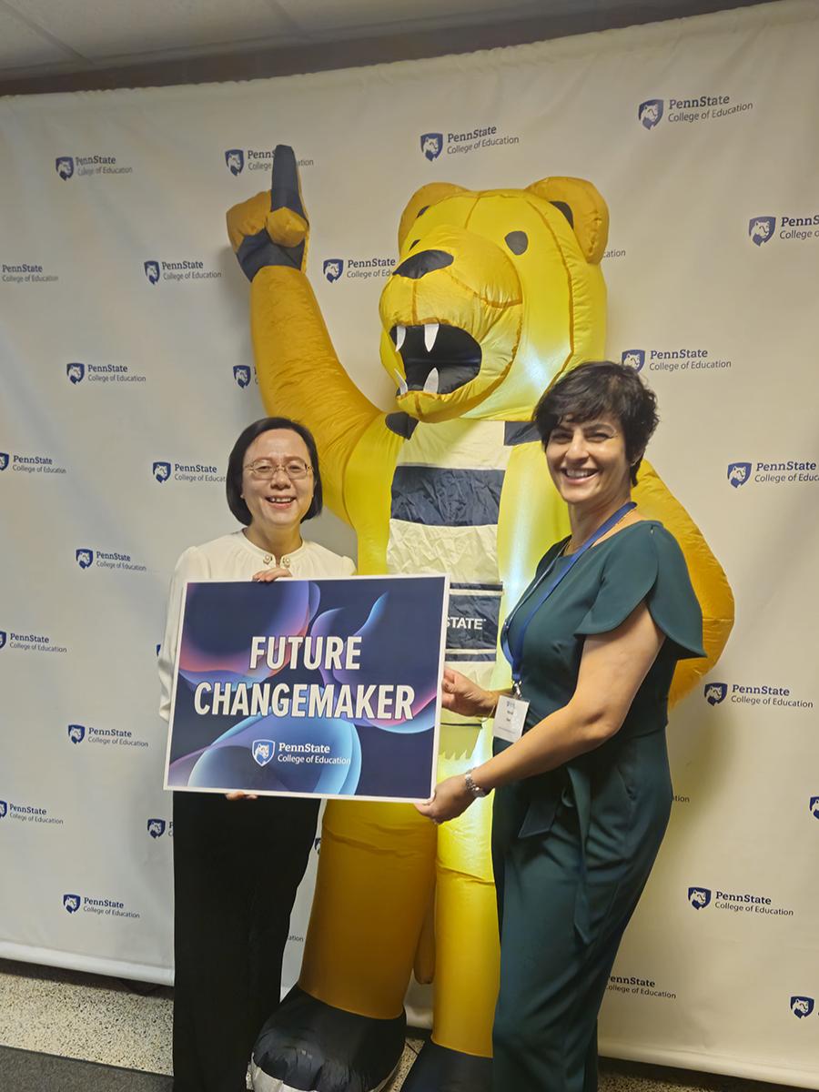 Two students pose with a sign and an inflatable Nittany Lion mascot.