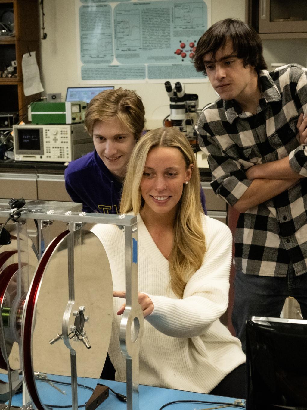 Three students lean over lab equipment. 