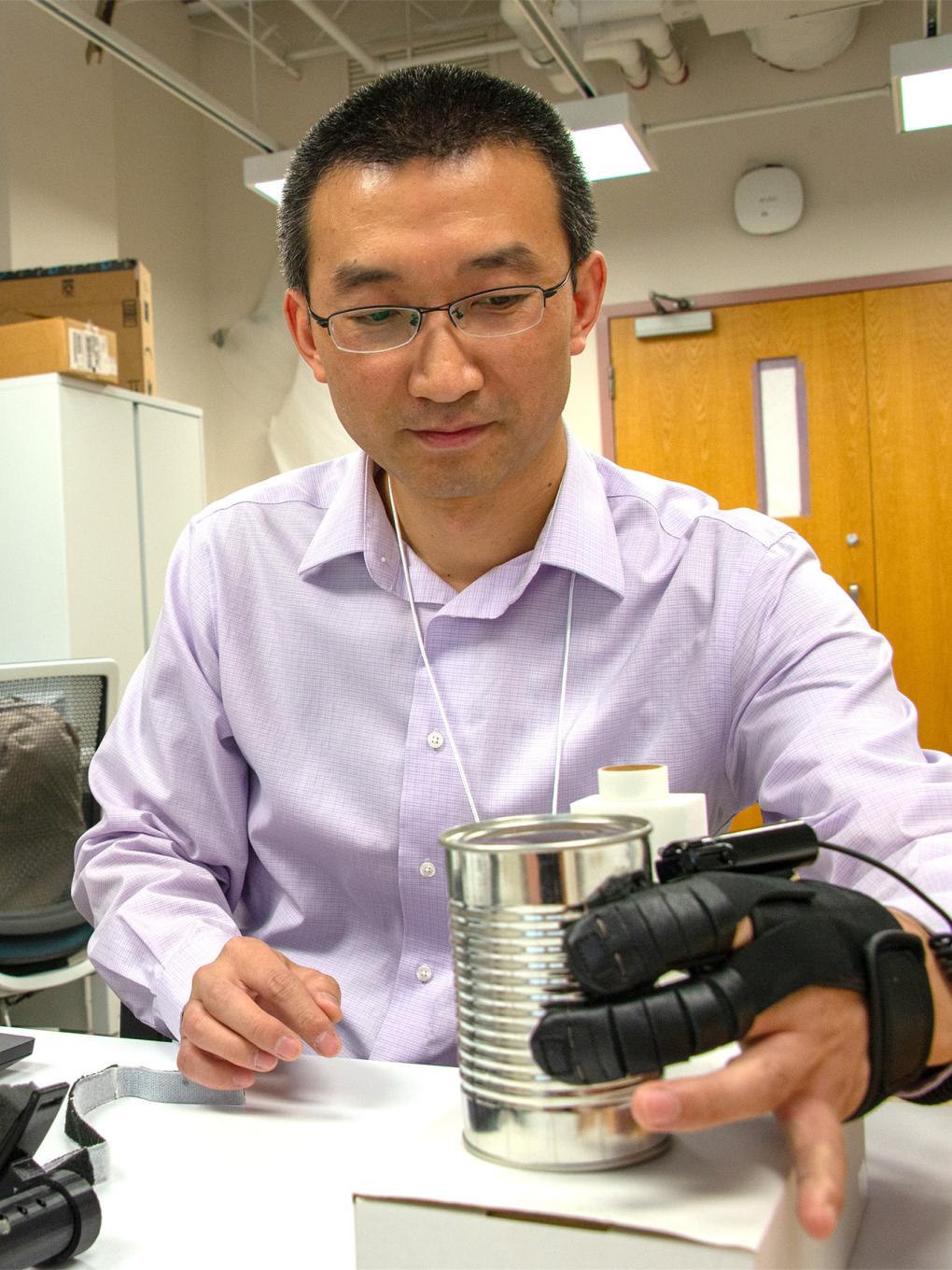 A person wearing a glove-like device lifts a can. 