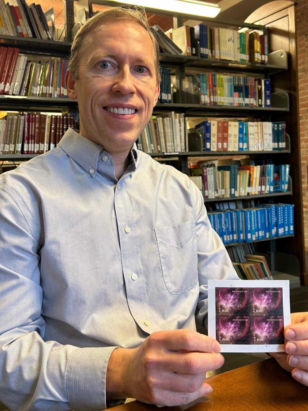 Image of Kevin Luhman holding a U.S. stamp with his image from the James Webb Space Telescope