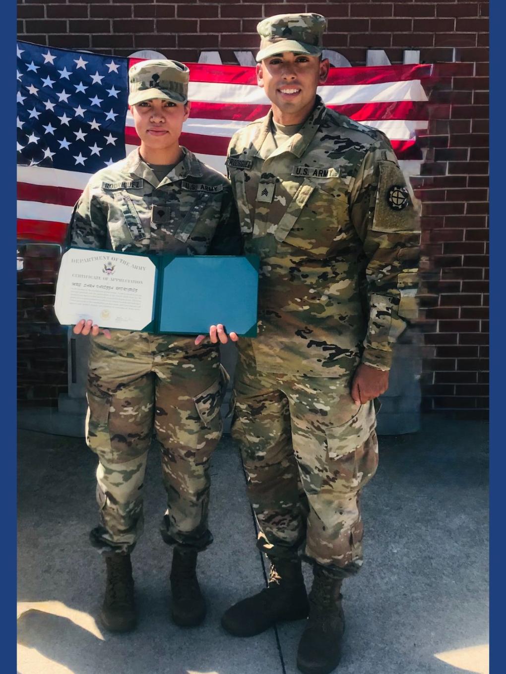 a woman in army fatigues holds a certificate standing next to a man in army fatigues