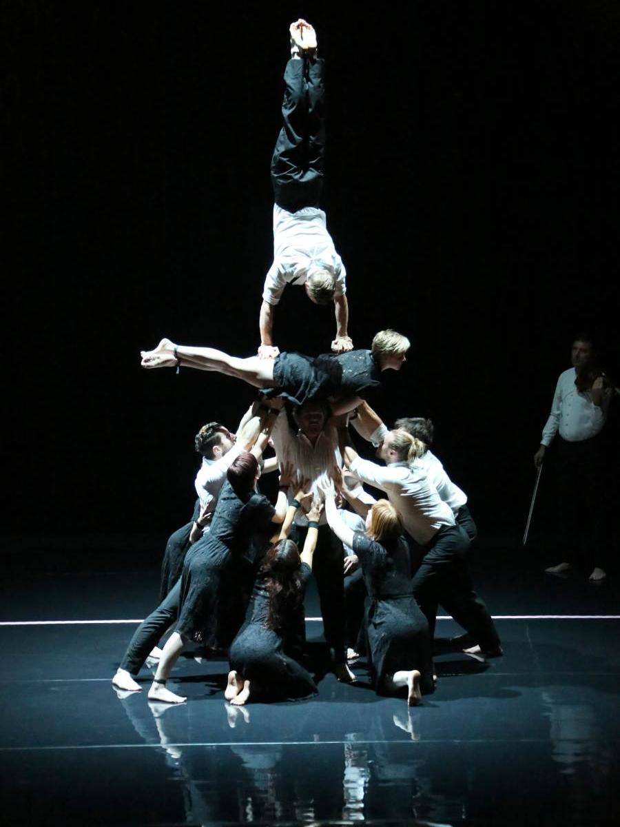 A group of Circa acrobats hold up another performer so his legs point straight up.