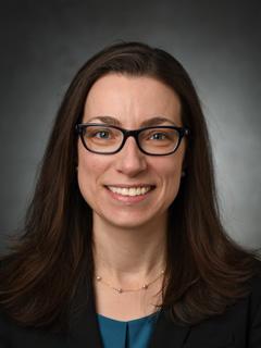 Head shot of a smiling woman with dark hair and glasses 