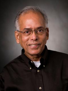 Man smiles at camera while wearing a black button down shirt and glasses