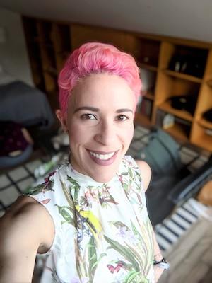 A professor with cropped pink hair smiles. 