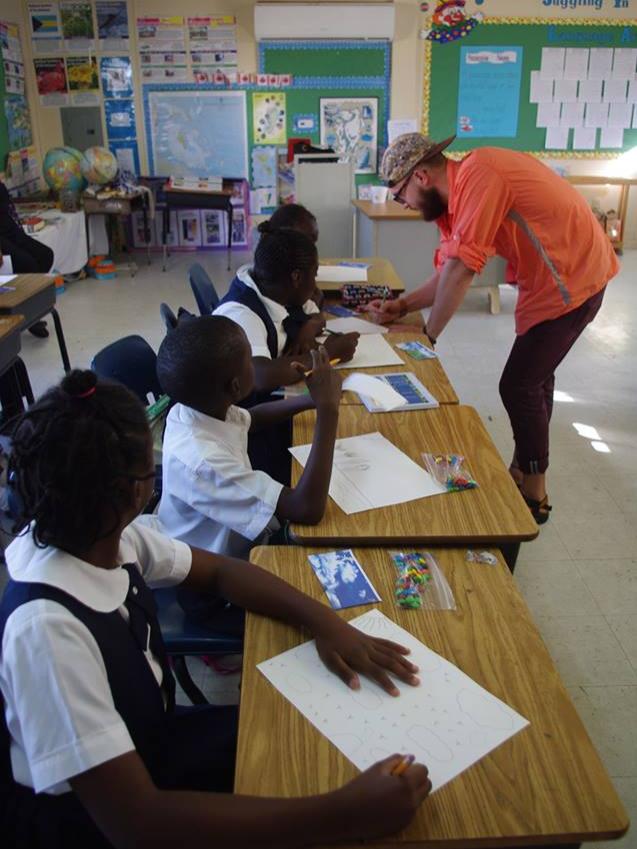 Penn State student Tyler Betz leans on a desk to teach children from San Salvador Island about the benefits of coral reefs.