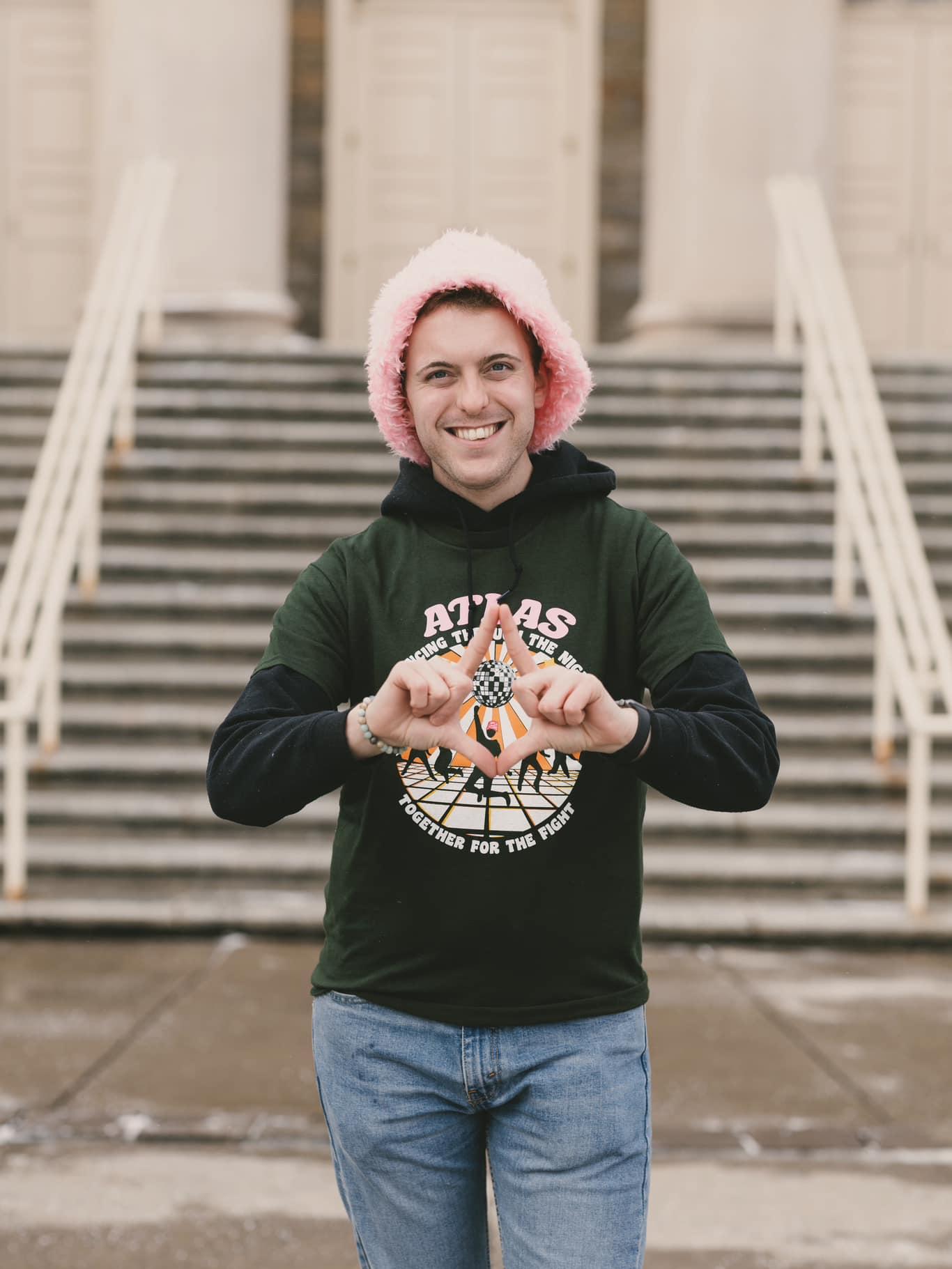 Young man with a pink, fuzzy hat standing in front of Old Main