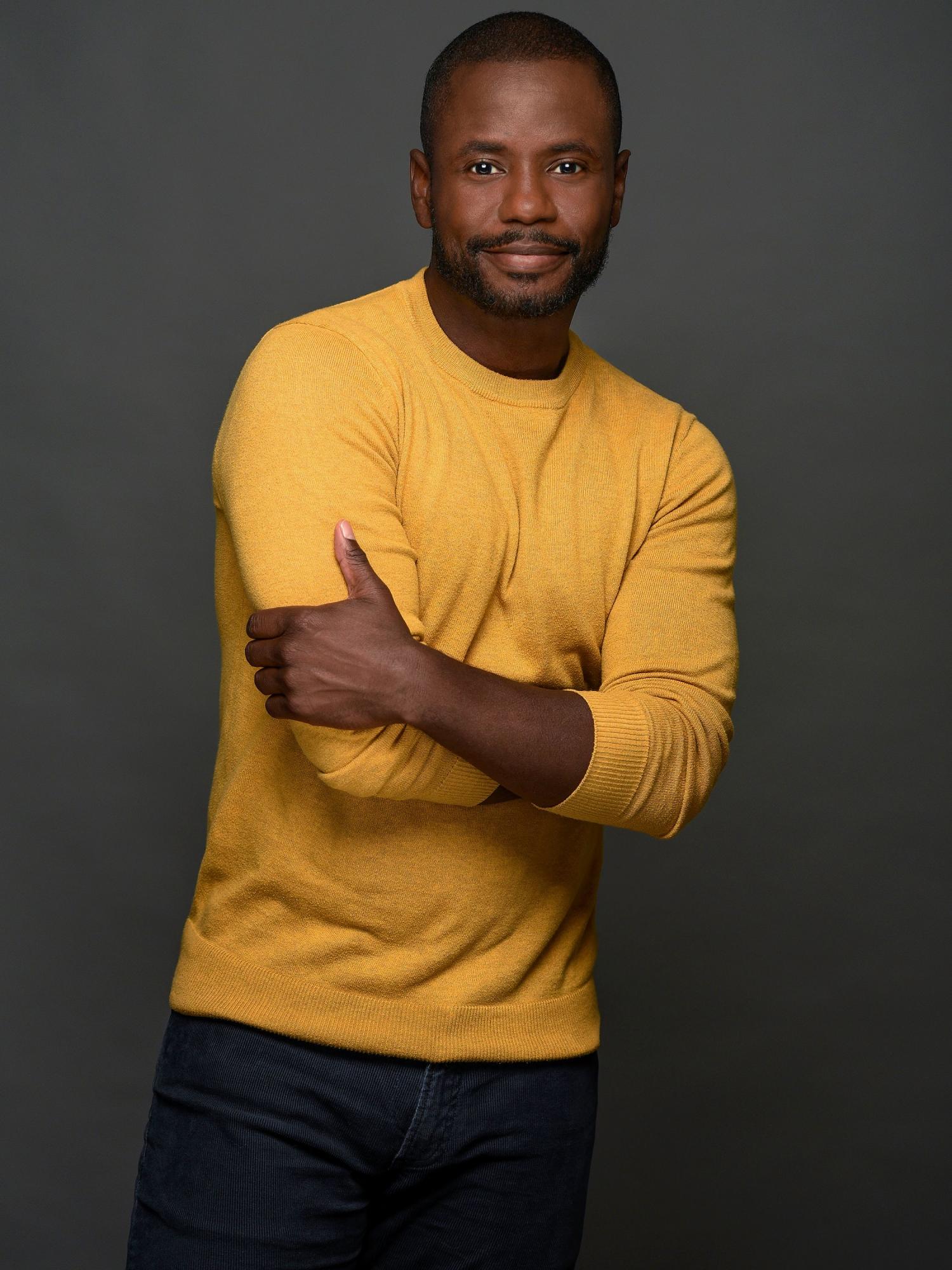 Black man with a yellow sweater posing casually
