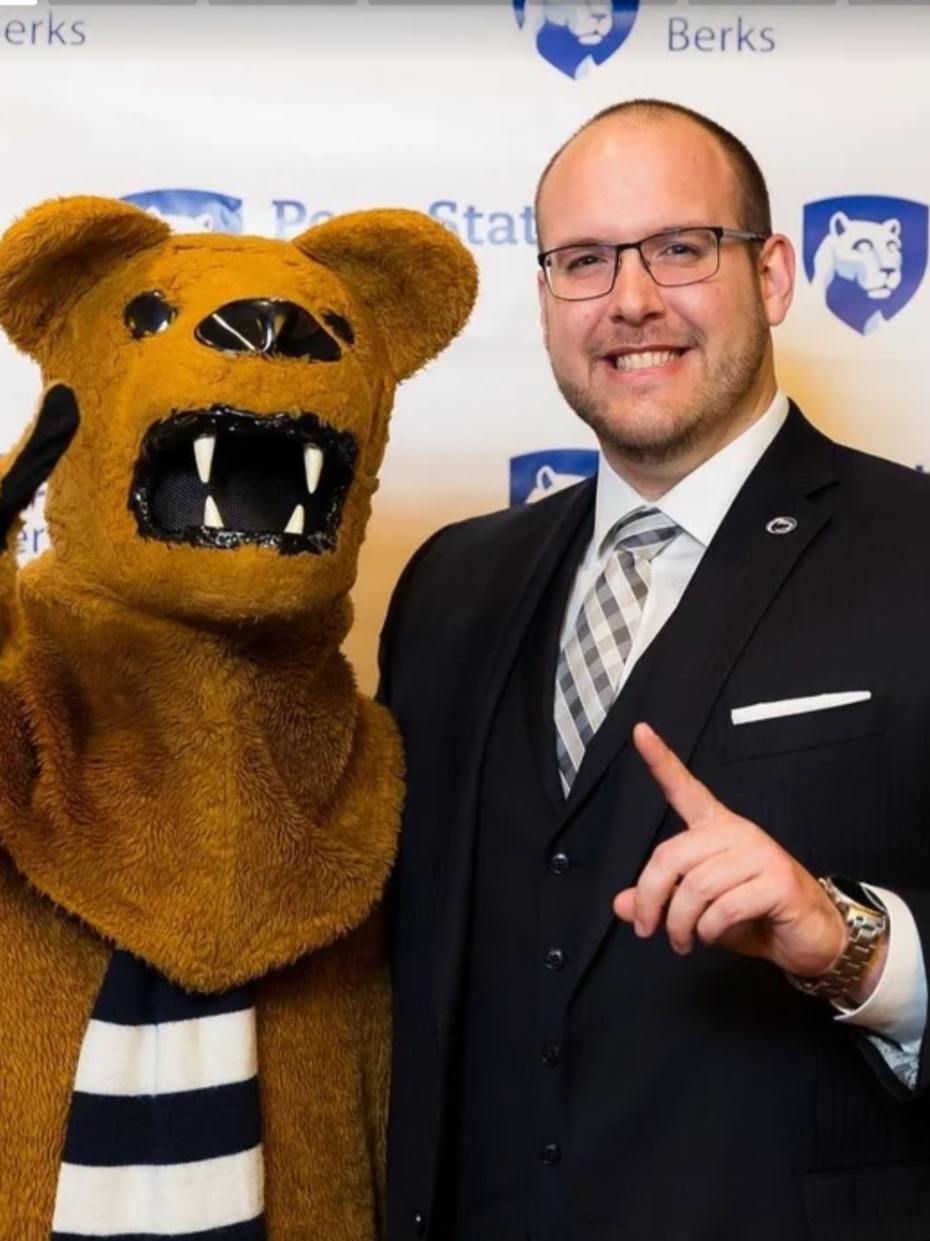 A person stands with the Nittany Lion, both hold up their index fingers