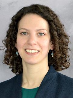 Headshot of a female, smiling and wearing a blue jacket with green blouse.