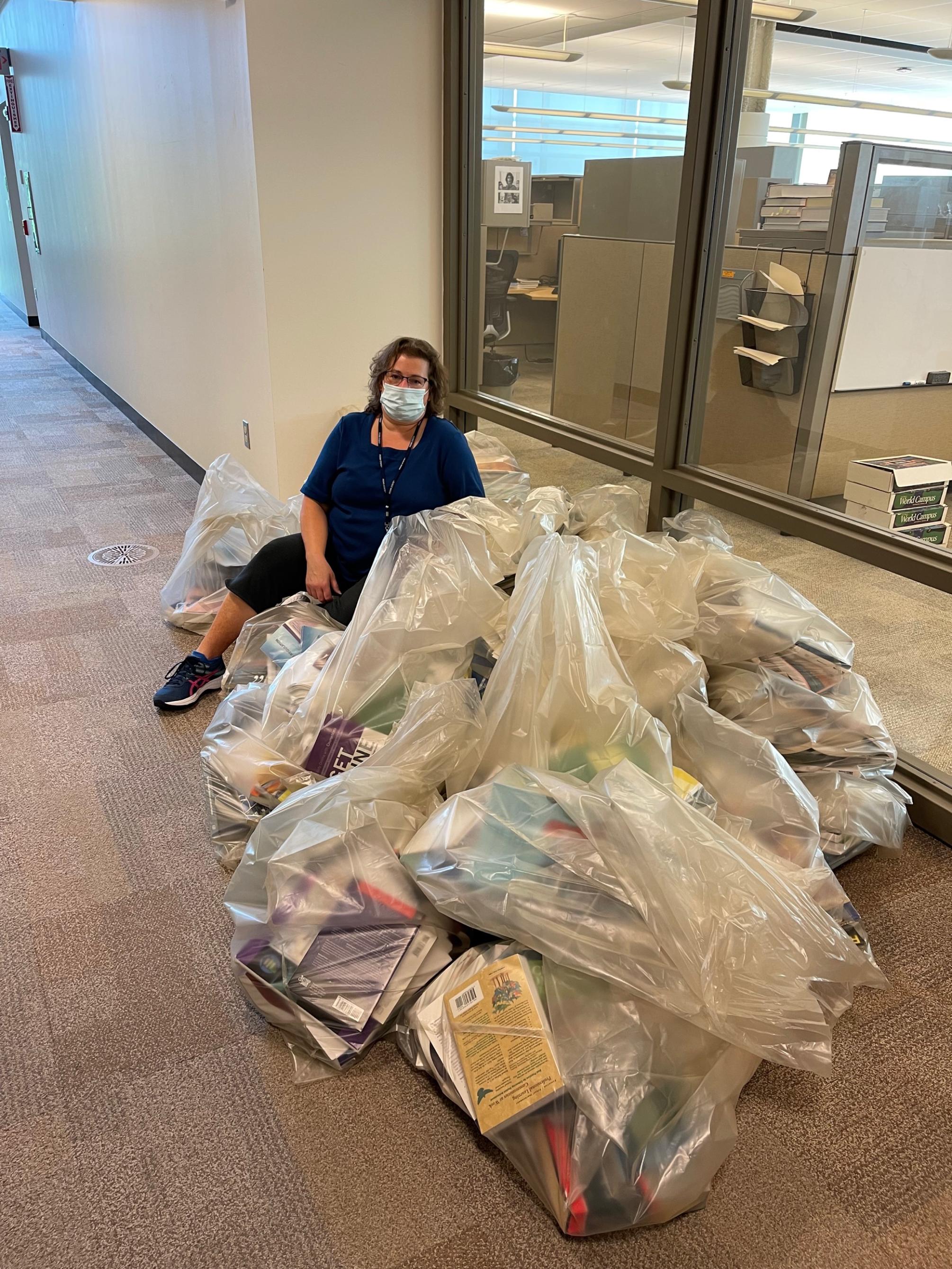 Suzzanne Clapper, manager of the instructional production specialists for Work Campus Learning Design, sits on the bags of recycled books.