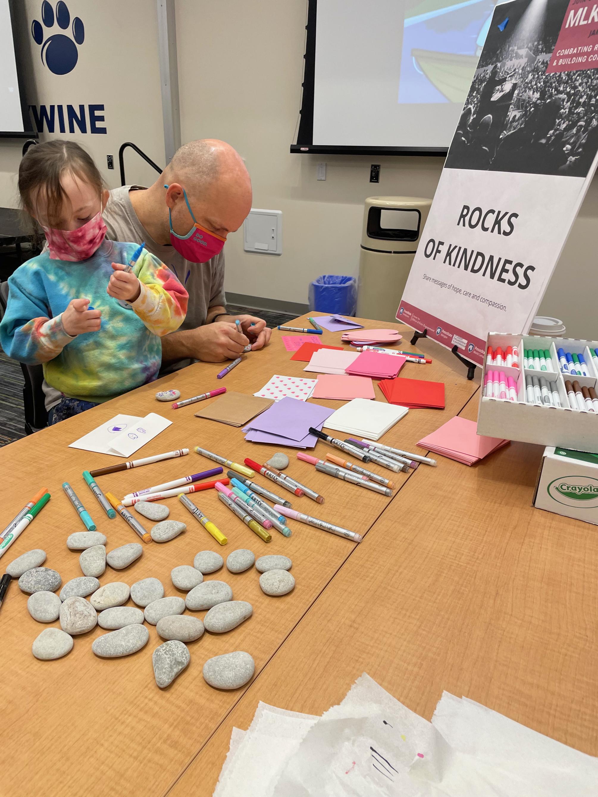 A father and daughter decorate rocks of kindness