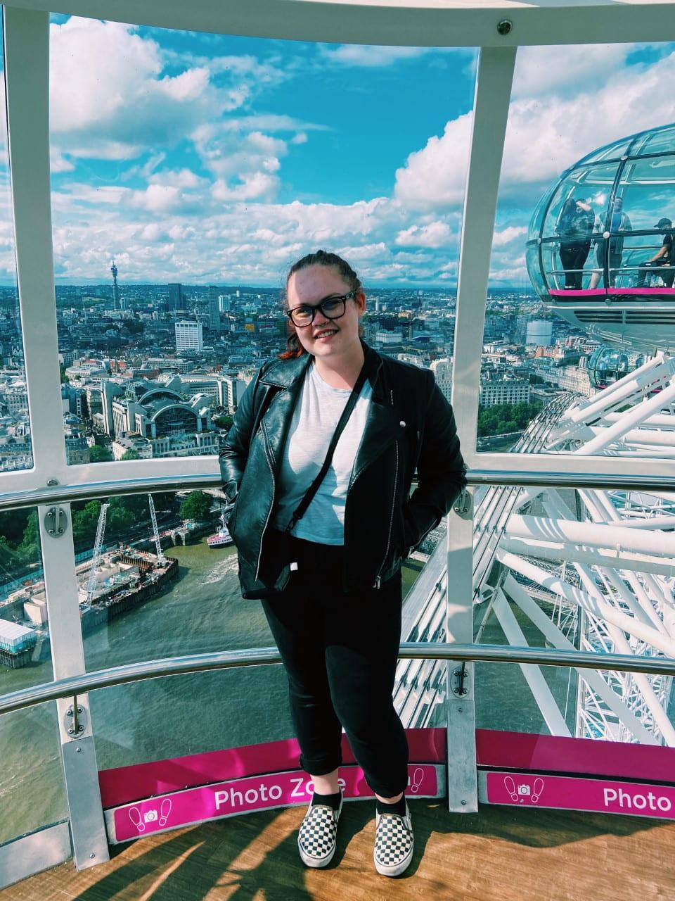 A girl poses in a glass dome Ferris wheel overlooking a city