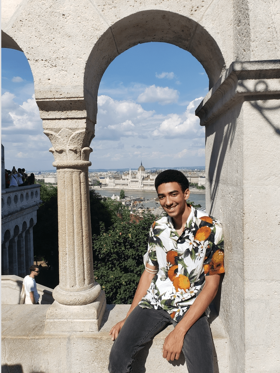 A man sits in an archway with a city behind him in the distance