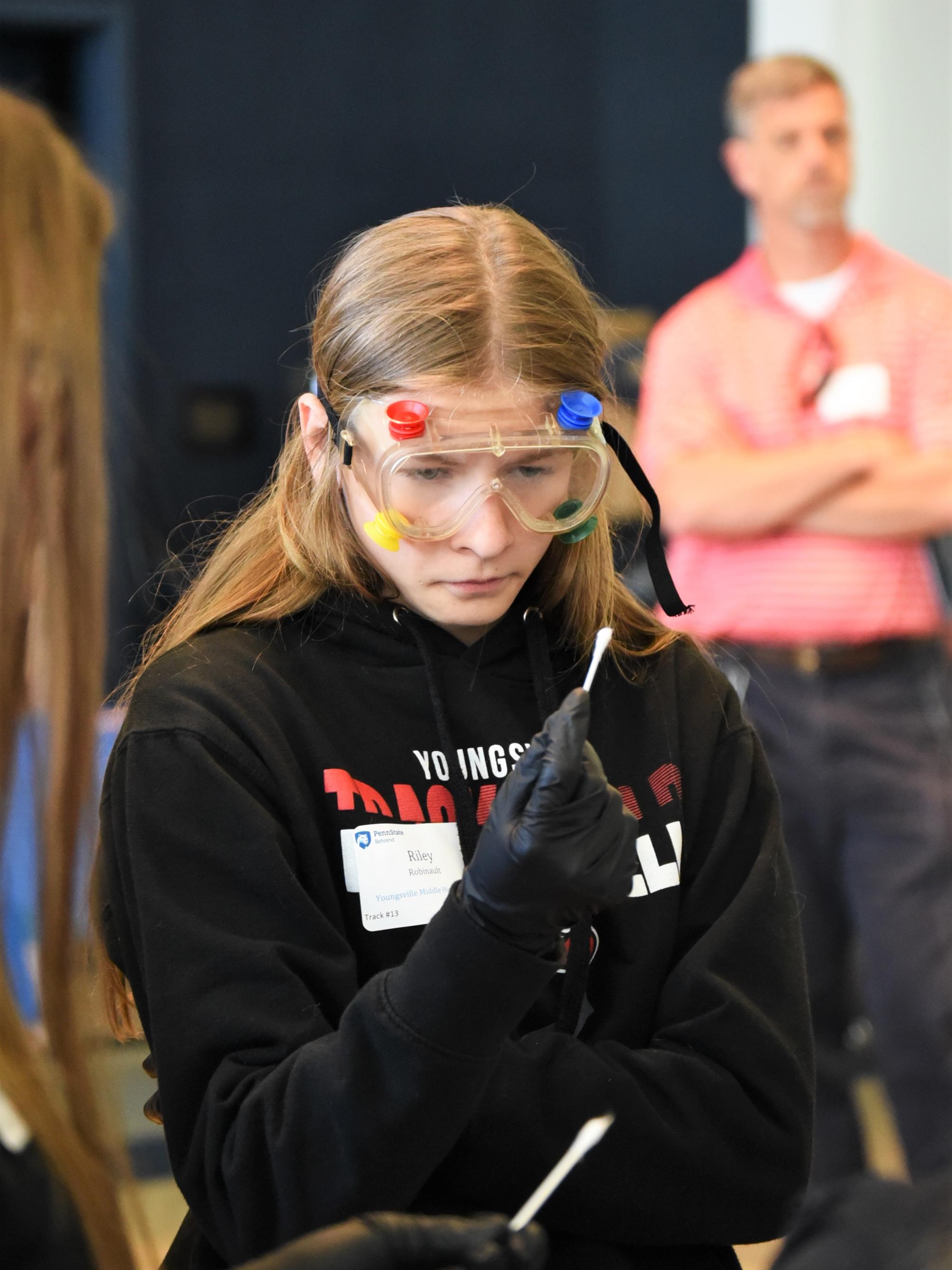 A female student looks closely at a cotton swab while investigating a staged crime scene.