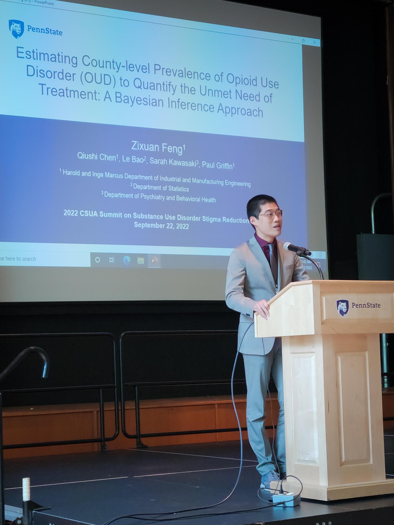 Zixuan Feng, a man in a grey suit, stands at the podium.