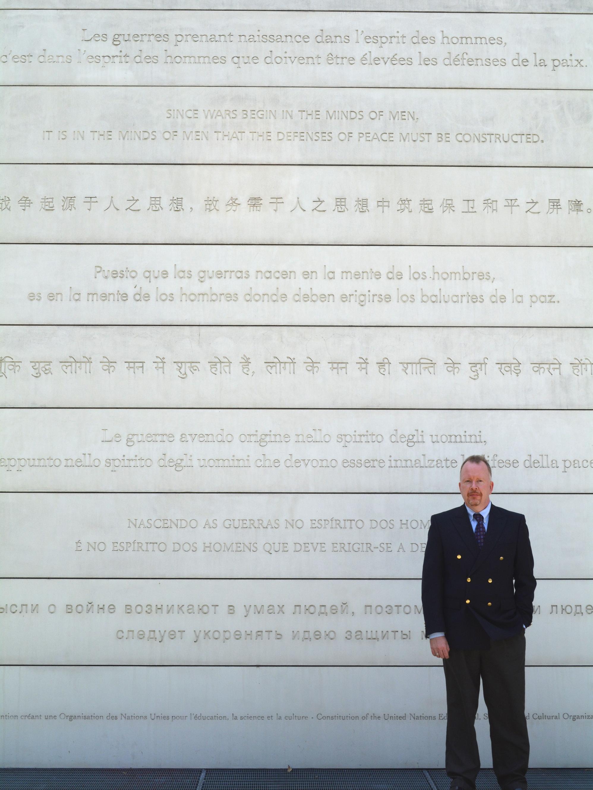 A man in front of the UNESCO Peace Wall with writing in various languages