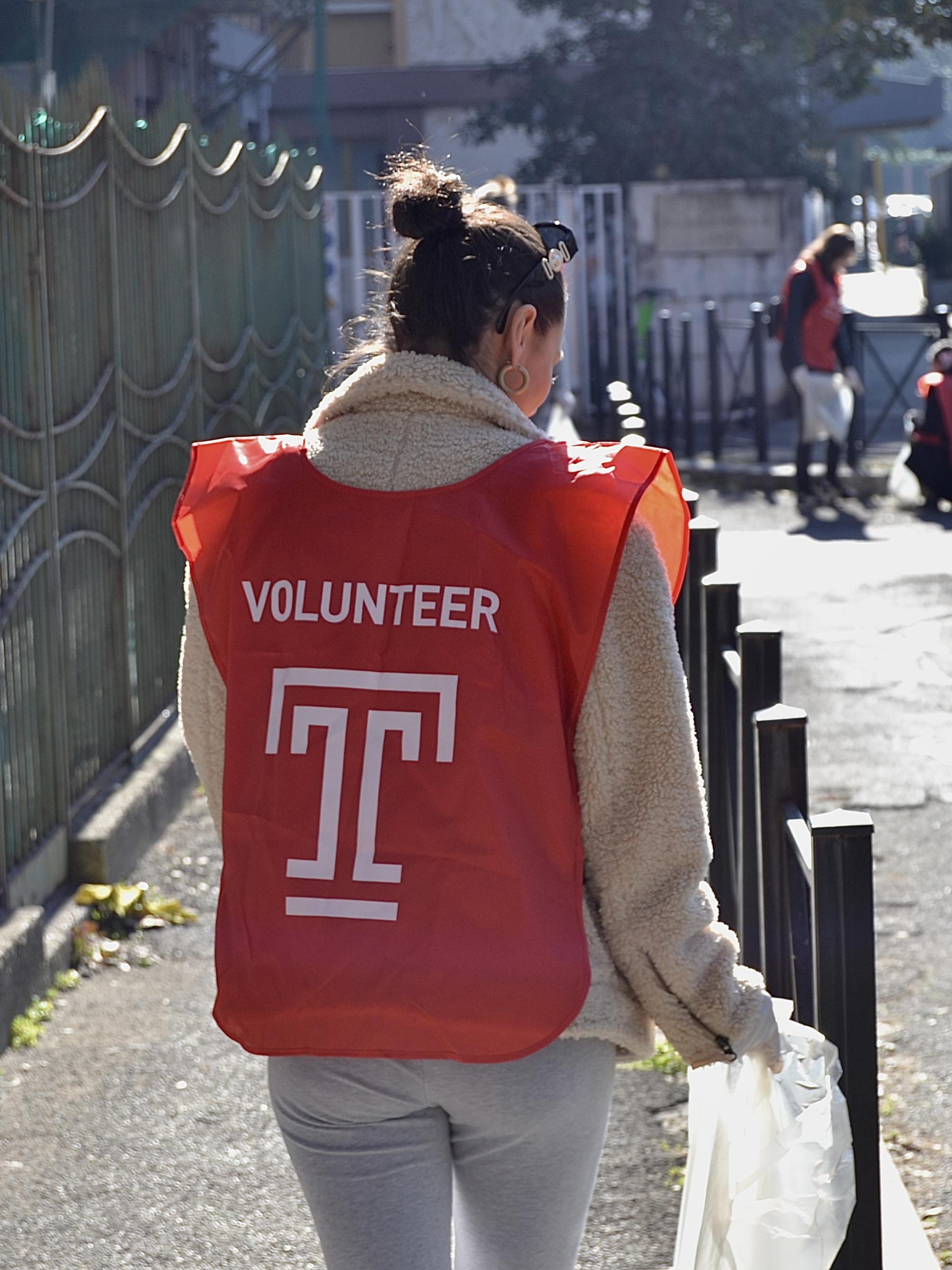 A student in a Temple overshirt cleaning up a street
